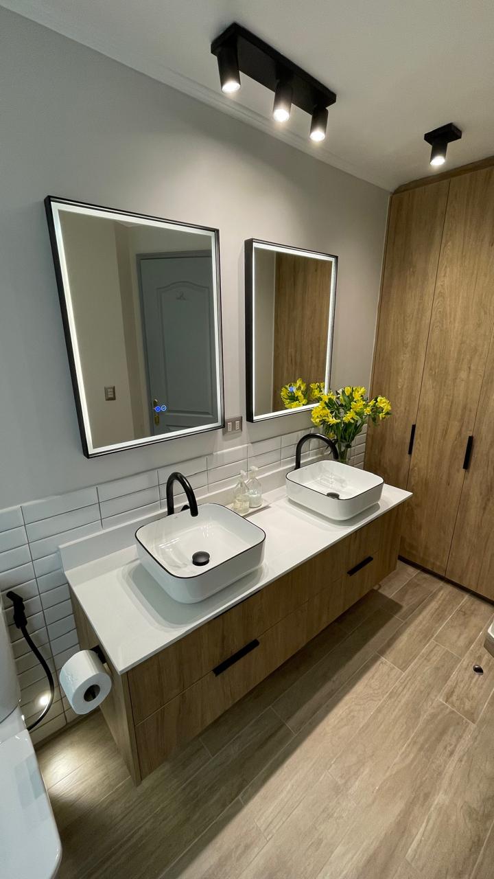 Baño con dos lavamanos de sobreponer, grifería negra, espejos con luz y vanitorio de madera
