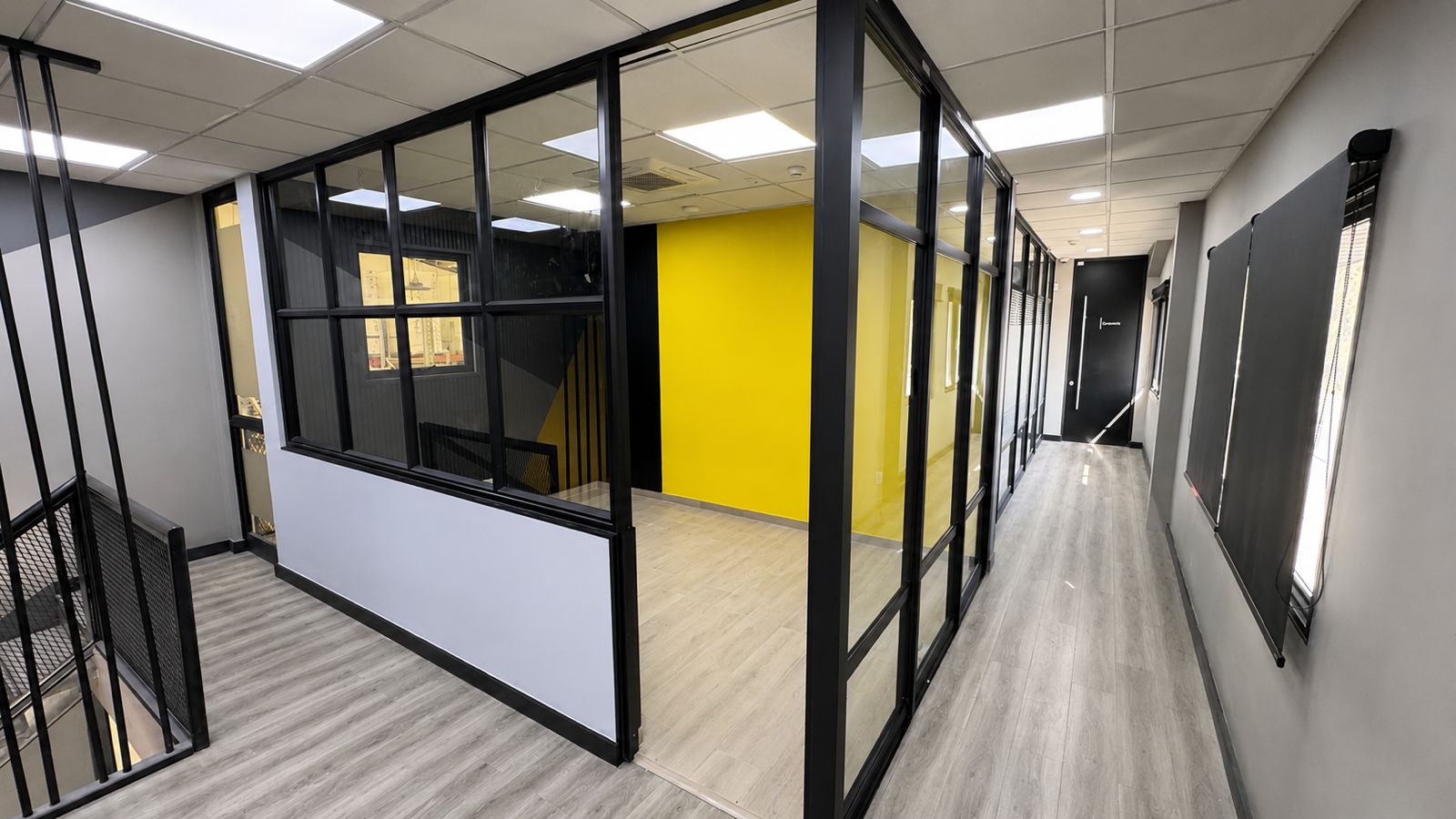 Oficinas Bertech: privados con tabiques vidriados de perfilería negra, muro amarillo y pasillo con piso de madera