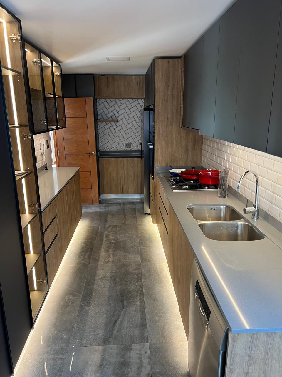Cocina en gris y madera con vitrinas iluminadas, cubierta de cuarzo e iluminación LED bajo los muebles