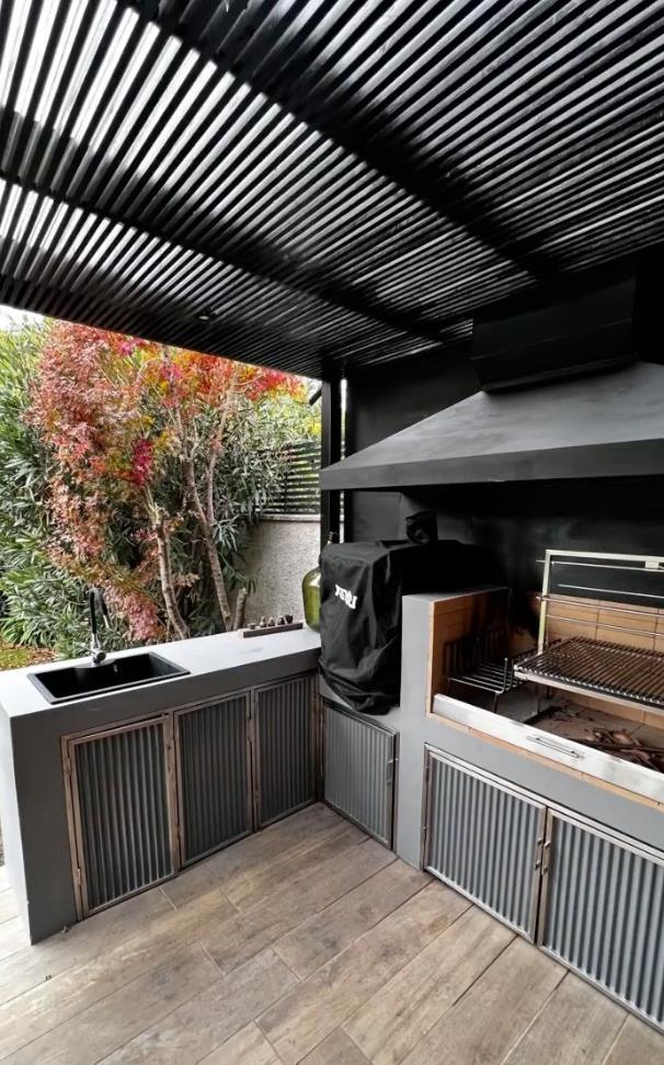Quincho exterior con pérgola de acero negro y parrilla empotrada