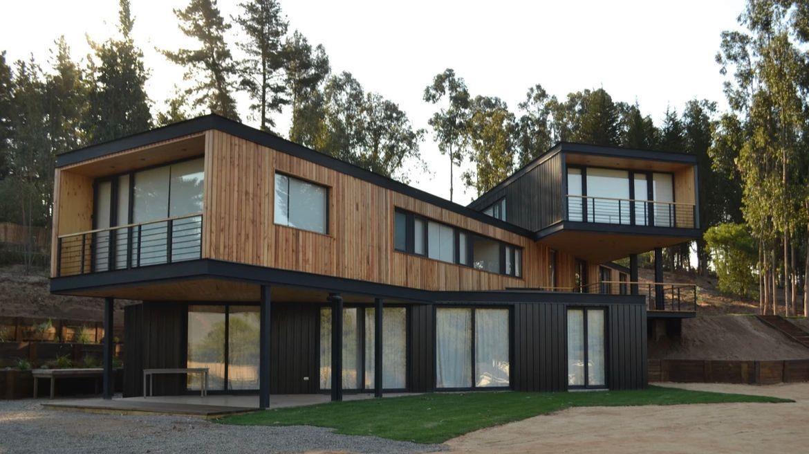 Vivienda de dos pisos en madera y acero negro construida en ladera, entre eucaliptos